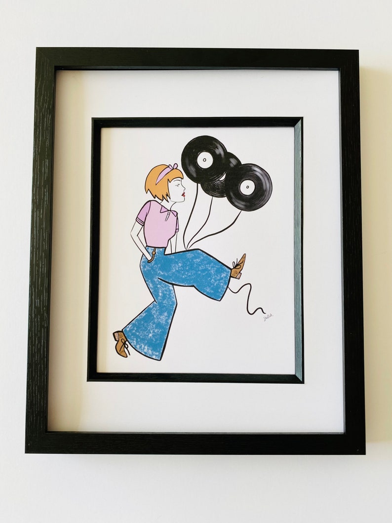 May include: A framed illustration of a woman with short blonde hair wearing a pink shirt and blue jeans. She is holding three black vinyl records as balloons. The illustration is signed "Julie".