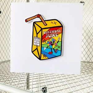 May include: A yellow and red birthday juice box with a cartoon character on the front. The character is a smiling face with a disco ball for a head. The text on the box says "Birthday Juice".