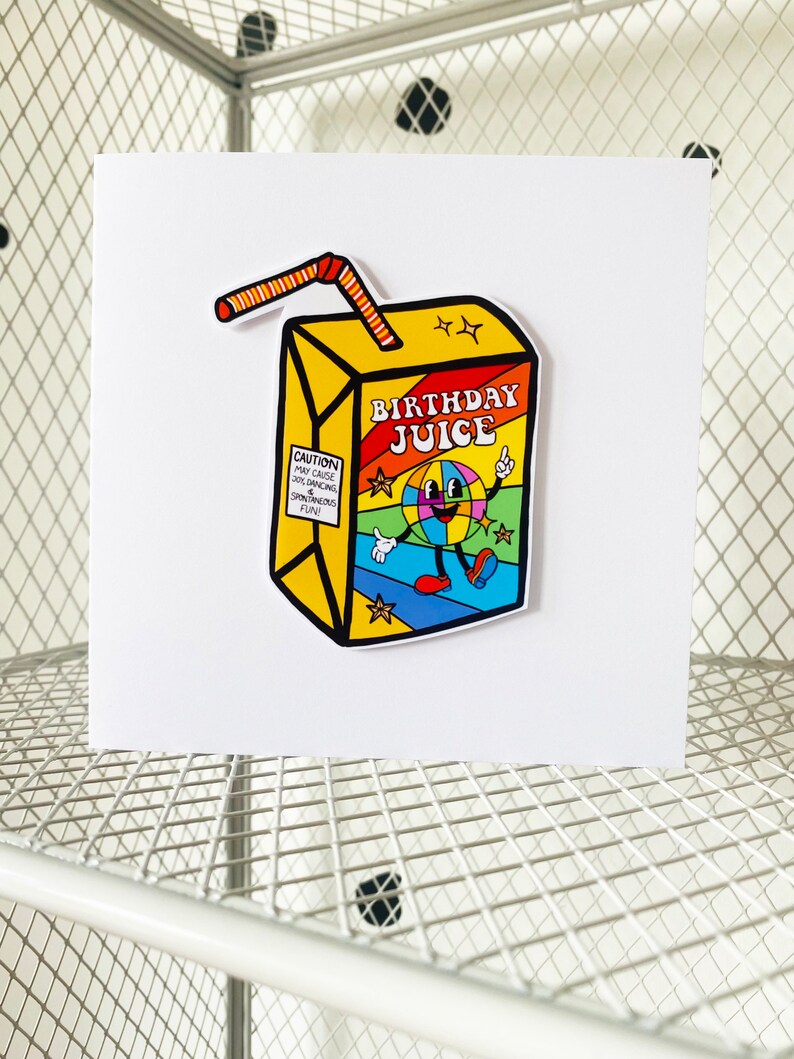 May include: A yellow and red birthday juice box with a cartoon character on the front. The character is a smiling face with a disco ball for a head. The text on the box says "Birthday Juice".