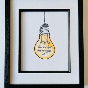 May include: A framed print with a yellow lightbulb drawn in black ink. The lightbulb has a quote inside that reads "There is a light that never goes out."