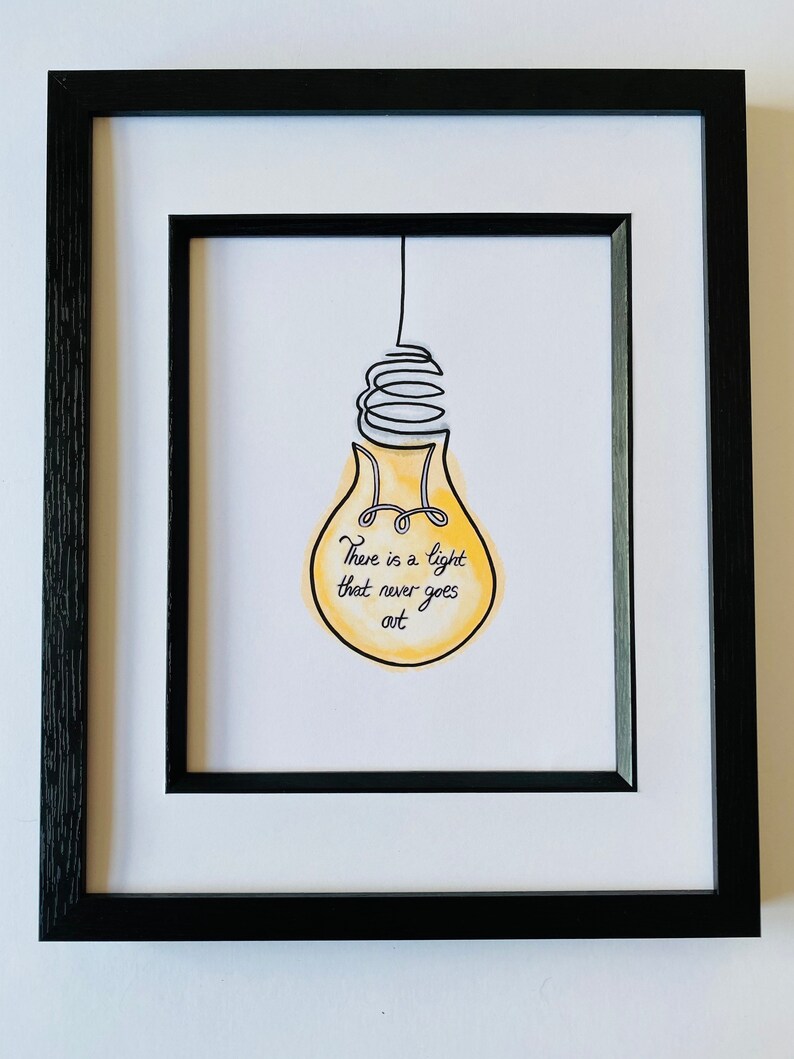 May include: A framed print with a yellow lightbulb drawn in black ink. The lightbulb has a quote inside that reads "There is a light that never goes out."