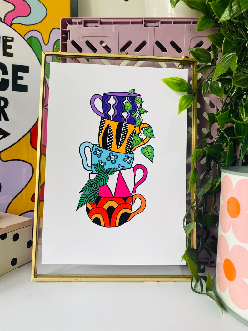 May include: A stack of four colorful mugs with geometric patterns and a leafy plant growing out of the top. The mugs are stacked in a tower, with the largest mug at the bottom and the smallest mug at the top. The mugs are all different colors and patterns, and the plant is green and leafy.