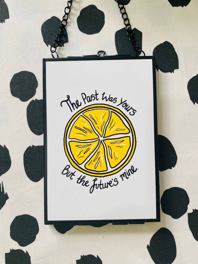 K&ouml;nnte beinhalten: Ein schwarzer gerahmter Druck mit wei&szlig;em Hintergrund und einer Illustration einer gelben Zitronenscheibe. Der Text lautet "The past was yours but the future's mine."