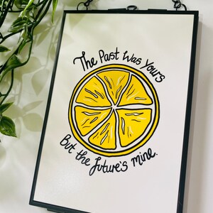 K&ouml;nnte beinhalten: Ein schwarzer gerahmter Druck mit einer gelben Zitronenscheibe und dem Text "The Past was Yours But the Future's mine."