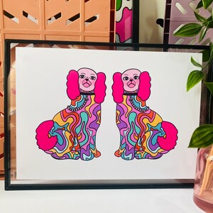 May include: A framed print of two colorful, psychedelic dogs with pink fur and black collars. The dogs are facing forward and have a swirling, abstract pattern on their bodies.