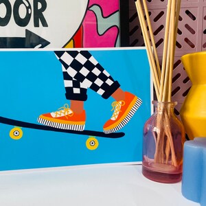 Pu&ograve; includere: Una gamba a scacchi blu e bianchi su uno skateboard con scarpe arancioni. Lo skateboard ha ruote gialle. Lo sfondo &egrave; di colore azzurro chiaro.