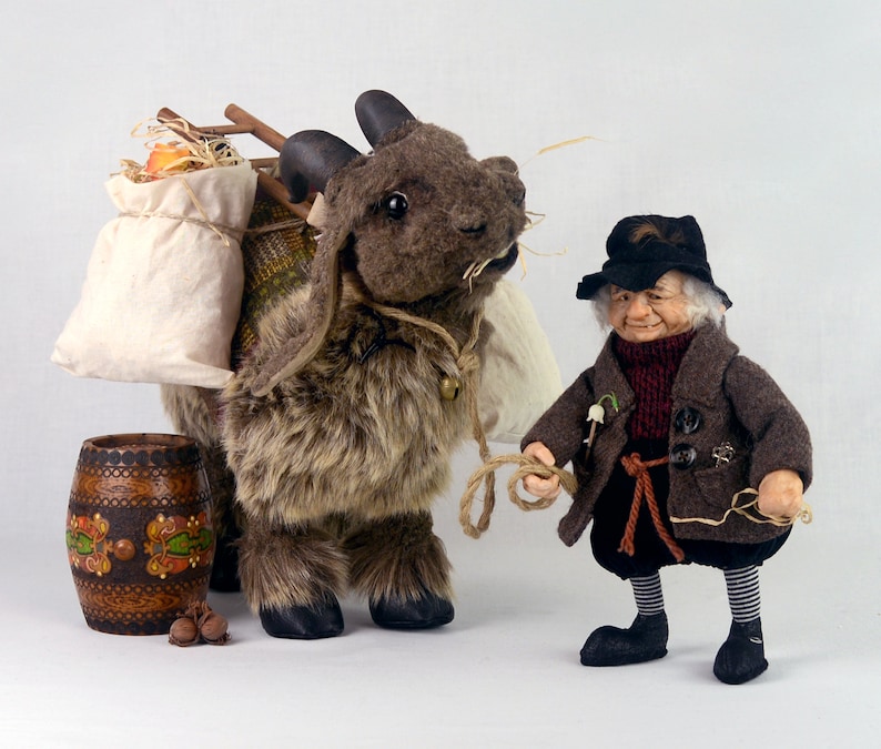 May include: A brown and white furry goat with a saddle and a bag on its back. A small, brown-haired gnome with a black hat and a brown coat is holding a rope attached to the goat.