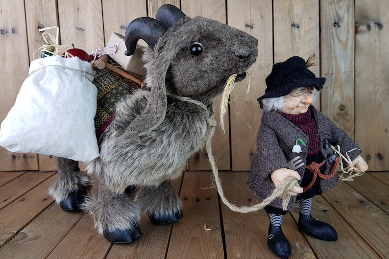 May include: A brown and gray stuffed goat with a white bag and other items on its back. A small, gray-haired gnome with a black hat and brown coat is holding a rope attached to the goat.