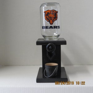 May include: A black wooden candy dispenser with a glass jar featuring a Chicago Bears logo. The jar has the word "BEARS" printed on it. The dispenser has a small black bucket underneath.