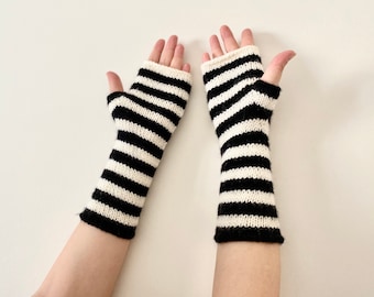 May include: A pair of black and white striped fingerless gloves. The gloves are knitted with alternating black and white horizontal stripes. The wrist and finger openings are finished with a solid black trim. The gloves are displayed against a white background.