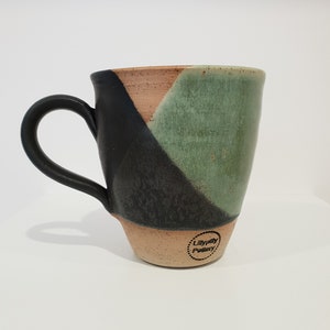 May include: A handmade ceramic mug with a black handle and a color-blocked design. The mug features sections of black, green, and tan. The bottom of the mug has the text "Lillypilly Pottery" in a circular design.
