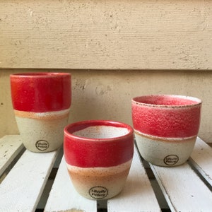 May include: Three red and white ceramic mugs with a speckled glaze. The mugs are different sizes and have the text "LillyPilly Pottery" stamped on the bottom.