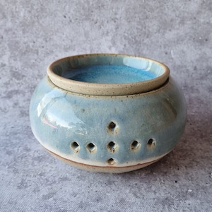 May include: A light blue ceramic wax warmer with a white rim and a light blue interior. The warmer has a series of small holes around the bottom edge.