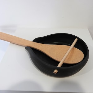 May include: A black ceramic spoon rest with a wooden spoon and a wooden stick resting inside.