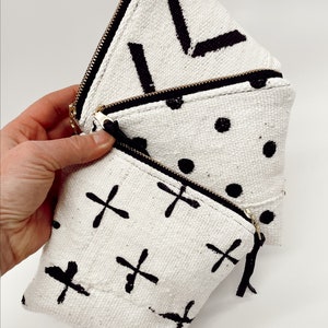 May include: Three white zippered pouches with black geometric patterns. The pouches are stacked on top of each other. The top pouch has a chevron pattern, the middle pouch has a polka dot pattern, and the bottom pouch has a cross pattern.