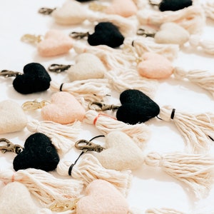 May include: A collection of felt heart keychains with tassels. The hearts are in black, pink, and white.