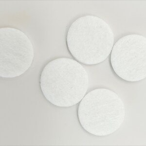 May include: Five white round felt pads, likely for furniture or other objects to prevent scratching.