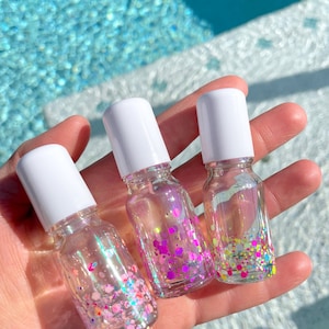 May include: Three clear glass bottles with white lids filled with iridescent glitter. The bottles are filled with different colors of glitter, including pink, purple, and green.