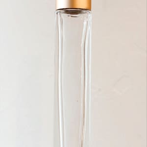 May include: A clear glass roller bottle with a gold metal cap. The bottle is empty and has a rectangular shape.