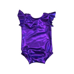 May include: A shiny, purple bodysuit with ruffled sleeves. The one-piece garment has a scoop neckline and is made of a metallic fabric. The bodysuit is designed for dance or gymnastics.