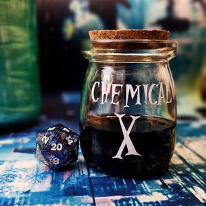 May include: A glass jar with a cork lid, labeled "CHEMICAL X" in white lettering, filled with a dark liquid. A multi-sided die with white numbers sits next to the jar. The background is a blurred blue and white pattern.