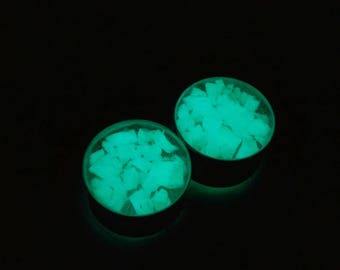 May include: Two round, green glow-in-the-dark ear gauges. The gauges are filled with small, irregular pieces of green material.