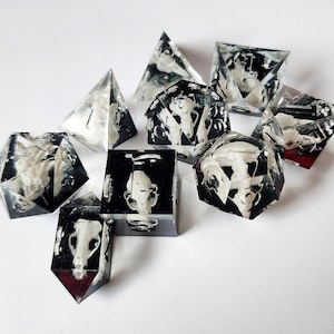 May include: Set of ten clear, multi-sided dice with black and white images of skulls and bones. The dice are made of a translucent material and have a glossy finish.