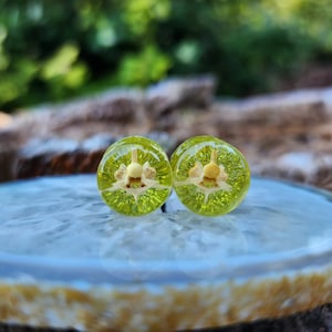 May include: Two round green glass earrings with a clear center and a white flower design inside.
