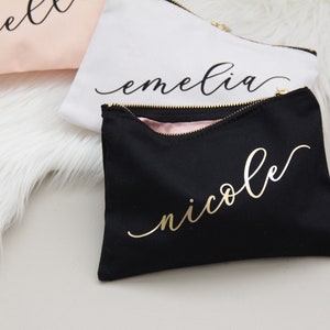 Puede incluir: Tres estuches con cremallera negros, blancos y rosas con letras doradas. Los estuches est&aacute;n personalizados con los nombres "Ella", "Emelia" y "Nicole".