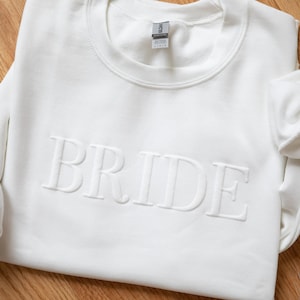 May include: White sweatshirt with the word "BRIDE" embossed in raised lettering.