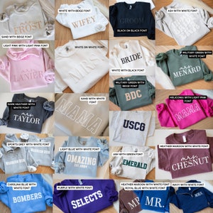 May include: A collection of 16 sweatshirts with various colours and text designs. The text includes names, phrases, and dates. The sweatshirts are arranged in a grid pattern.