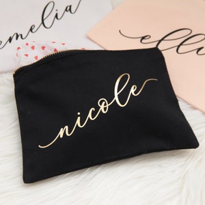 Puede incluir: Bolsa de maquillaje de lona negra con cremallera dorada y el nombre "nicole" escrito en letras doradas.
