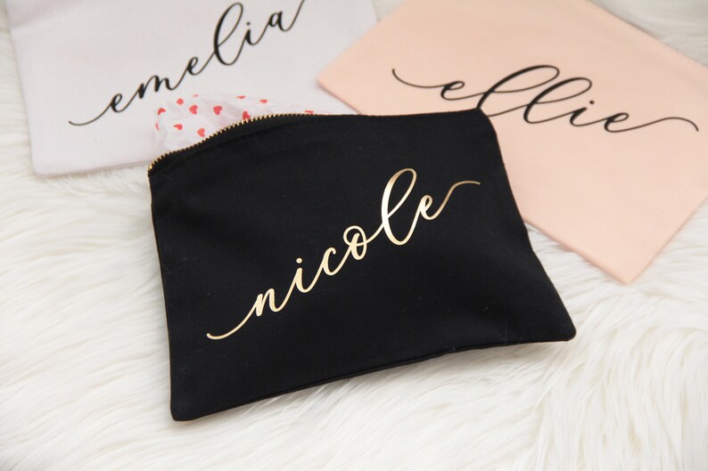 Puede incluir: Bolsa de maquillaje de lona negra con cremallera dorada y el nombre "nicole" escrito en letras doradas.