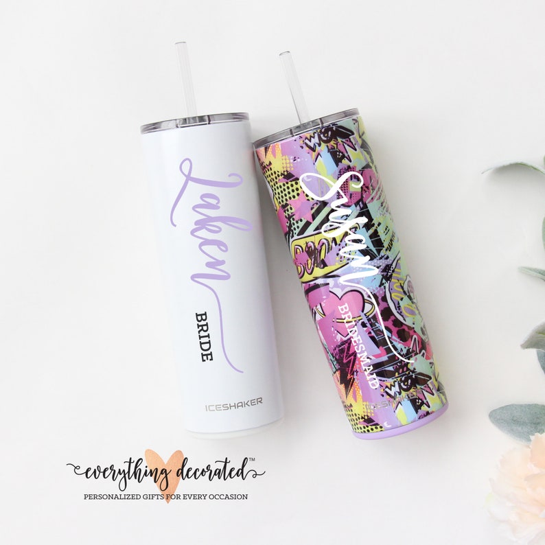 May include: Two stainless steel tumblers with lids and straws. The tumbler on the left is white with the word "Taken" and "Bride" written in purple script. The tumbler on the right has a colorful, graphic print with the word "Susan" and "Bridesmaid" written in white.
