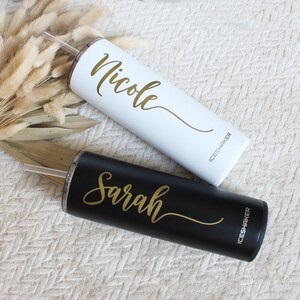 May include: Two stainless steel tumblers with lids and straws. One tumbler is white with the name "Nicole" in gold lettering and the other is black with the name "Sarah" in gold lettering. Both tumblers have the word "ICESHAKER" printed on the side.