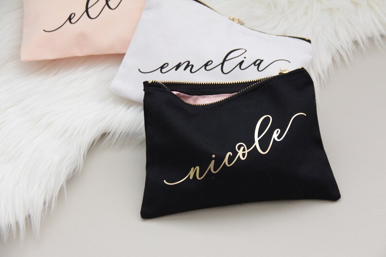 Puede incluir: Tres estuches con cremallera negros, blancos y rosas con letras doradas. Los estuches est&aacute;n personalizados con los nombres "Ella", "Emelia" y "Nicole".