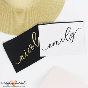 Puede incluir: Dos bolsas de lona negra con cremallera y letras doradas y negras. Las bolsas est&aacute;n personalizadas con los nombres "Emily" y "Nicole".