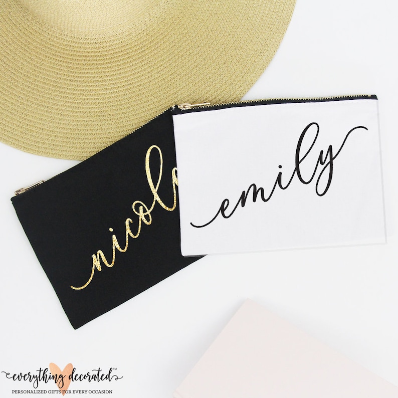 Puede incluir: Dos bolsas de lona negra con cremallera y letras doradas y negras. Las bolsas est&aacute;n personalizadas con los nombres "Emily" y "Nicole".