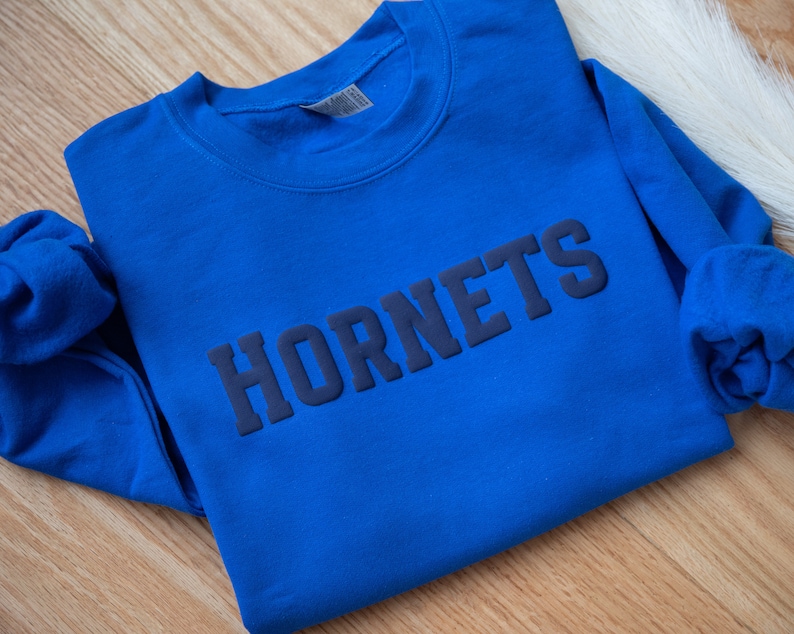 Puede incluir: Una sudadera azul real con la palabra "HORNETS" impresa en azul oscuro en la parte delantera.
