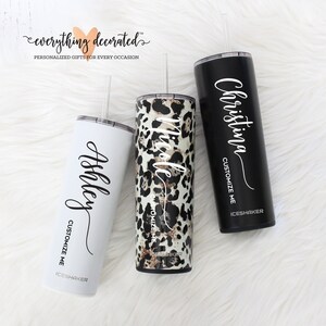 May include: Three stainless steel tumblers with personalized names, "Ashley", "Nicole", and "Christina". Each tumbler has a black lid and a straw. The tumbler on the left is white, the middle tumbler has a leopard print design, and the tumbler on the right is black.