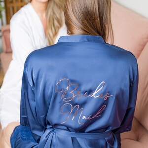 May include: A blue satin robe with the words "Brides Maid" written in rose gold lettering on the back.