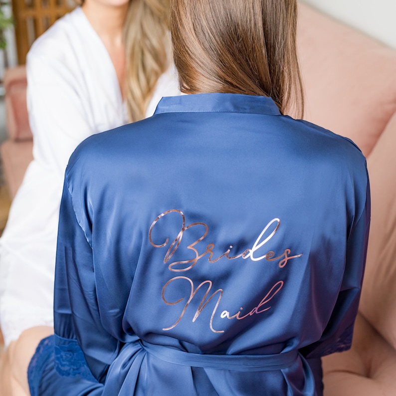 May include: A blue satin robe with the words "Brides Maid" written in rose gold lettering on the back.
