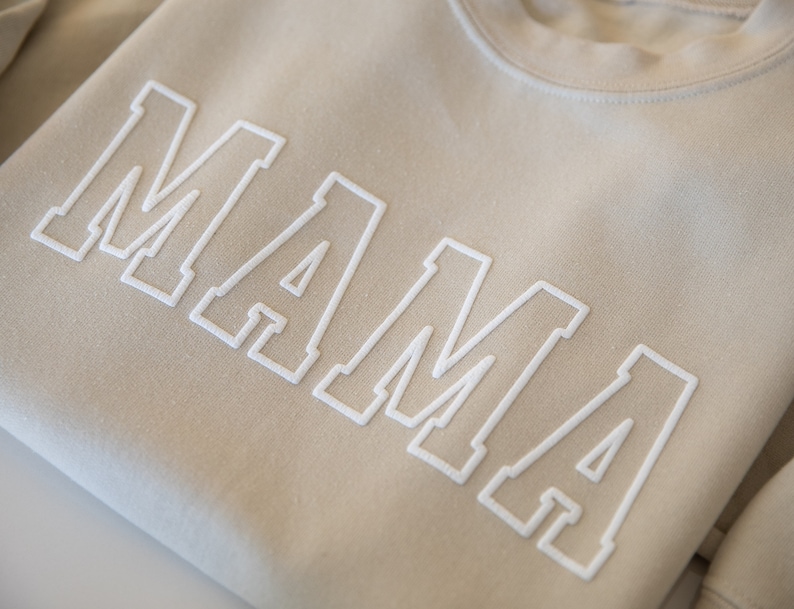 May include: A beige sweatshirt with the word "MAMA" in white outlined letters.