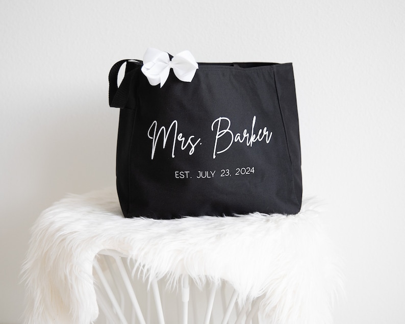 May include: Black canvas tote bag with white text that reads "Mrs. Barker EST. JULY 23, 2024".