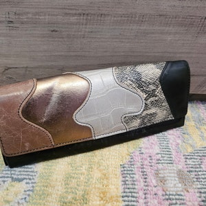 May include: A black leather wallet with a patchwork design. The wallet features different colored leathers, including brown, gold, and white. The wallet has a snakeskin pattern on one side.