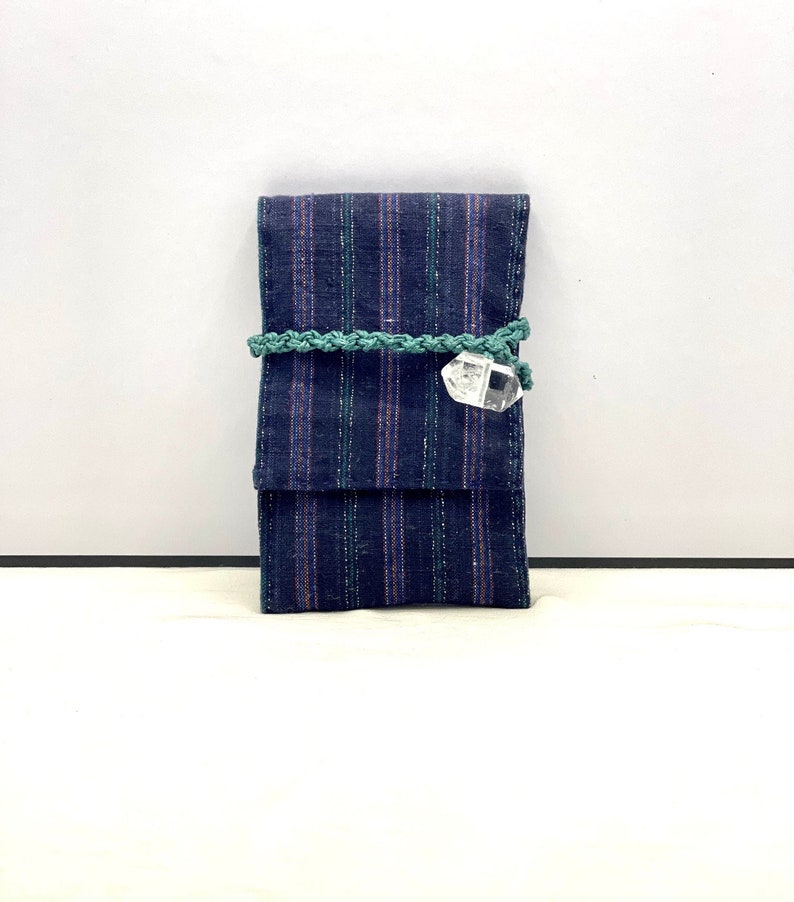 Op de afbeelding: Een blauwe en groene gestreepte stoffen tasje met een kristallen hanger. Het tasje is vastgebonden met een groen koord.