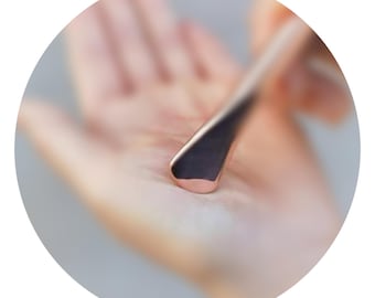 May include: A close-up of a rose gold metal tool with a flat, angled blade. The tool is held in a person's hand, with the focus on the tool's polished surface and rounded tip. The background is blurred.