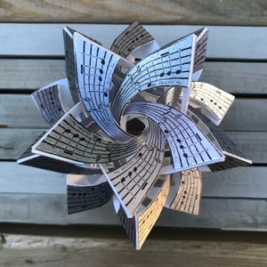 May include: A silver and white paper star with musical notes printed on each point. The star is folded into a three-dimensional shape.