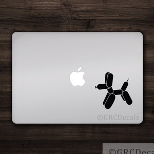Puede incluir: Una pegatina en blanco y negro de un perro de animal de globo en una computadora portátil plateada. La pegatina se coloca junto al logotipo de Apple en la computadora portátil.