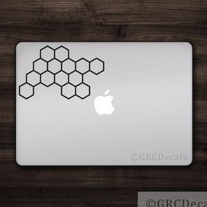 May include: A silver laptop with a black honeycomb design sticker on the top left corner. The Apple logo is visible on the right side of the laptop. The laptop is on a wooden surface.